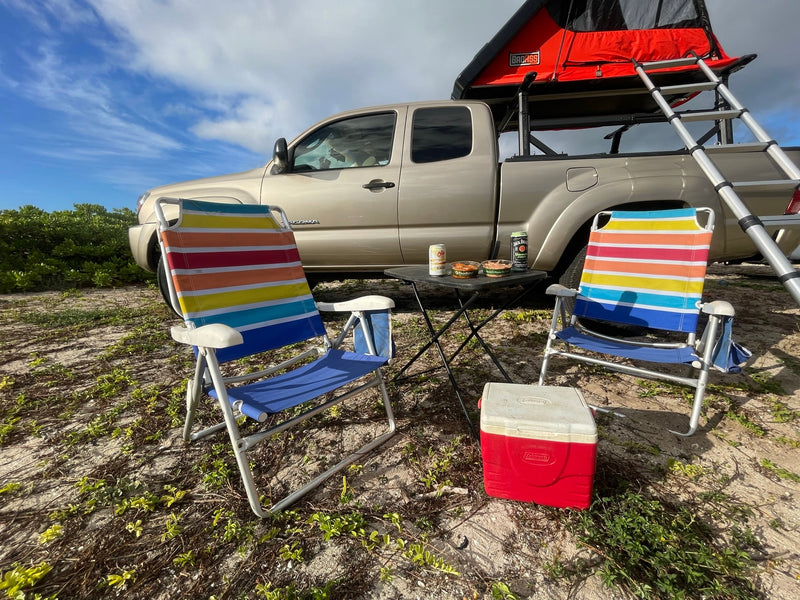 Enjoying an RV rental setup: a truck with rooftop tent, chairs, cooler, & snacks on a sandy campsite. — photo 10