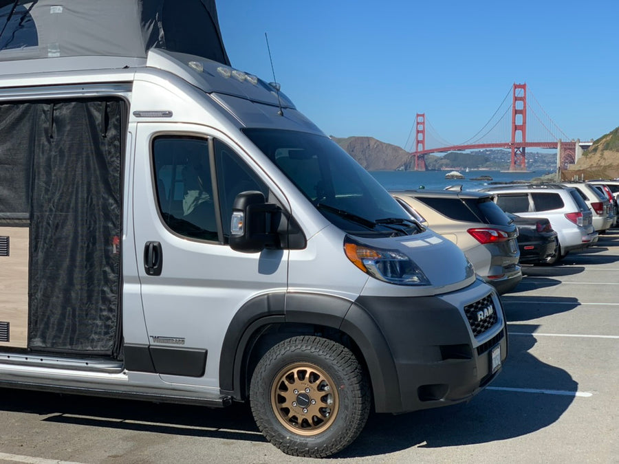 Silver pop-top RV rental van parked, with the iconic Golden Gate Bridge visible in the sunny background.