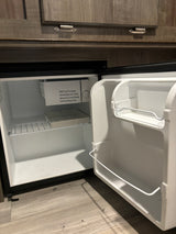 Inside an RV rental, a compact, open mini-fridge with white interior, wire shelf, and ice cube tray. Safety warning visible.