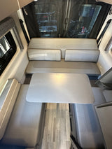 Explore this RV rental's inviting dinette, featuring light-toned cushioned benches, a central table, and wood-look flooring.