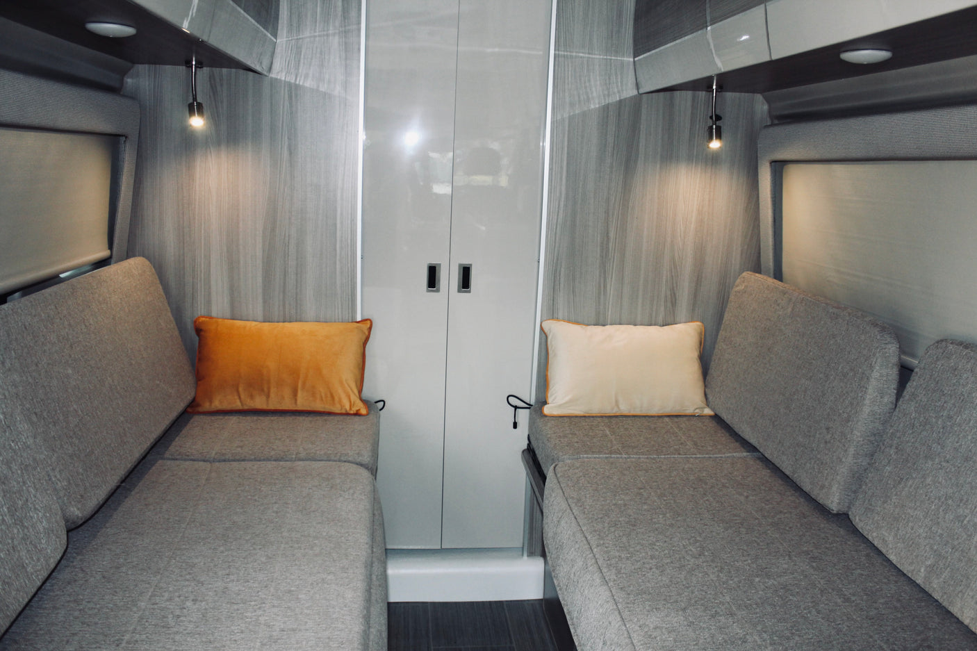 Modern RV rental interior: cozy facing benches with pillows, reading lights, and central storage.