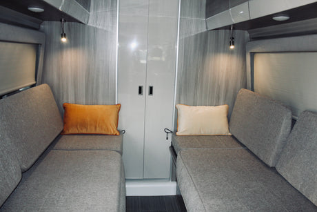 Modern RV rental interior: cozy facing benches with pillows, reading lights, and central storage.