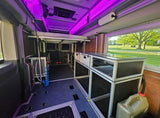 Interior of a customizable rv rental, a modular van conversion with bed, cabinets, and ambient purple lighting.