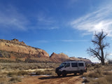Custom camper van, ideal for RV rental adventures, parked on a dirt road in a vast, arid landscape with cliffs.