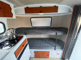 This RV rental's compact interior features bunk beds with dark cushions, a small kitchen with a stove and kettle.