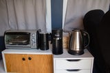 An RV rental compact kitchen counter features a toaster oven, Karesie coffee maker, Topvit kettle, and storage units.