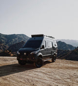 Explore off-road with this rugged Mercedes Sprinter rv rental. Dark van on a dirt path with majestic mountains under a bright sky.