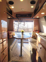 Cozy RV rental interior: A bright dinette with light wood cabinetry, comfortable benches, and a large window view for travel.