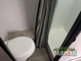 RV rental bathroom: Compact design features a white toilet and an adjacent shower stall with a striped curtain.