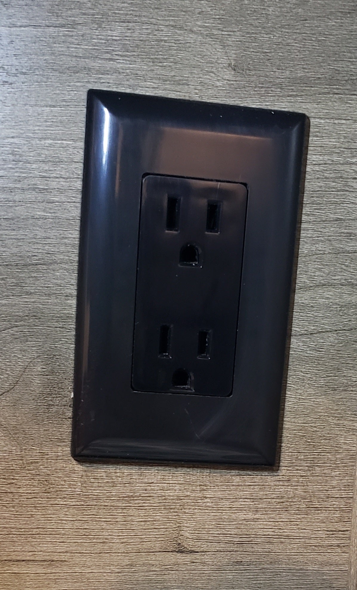 A dark, two-receptacle electrical outlet is flush on a wood-grain panel. Found in an RV rental for your devices.