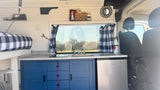This **RV rental** features a cozy kitchenette with sink/stove, fridge, blue cabinets, and a bed with checkered bedding.