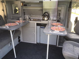 RV rental interior: organized kitchen with sink, stove, and fridge, plus two dining tables set for compact travel meals.