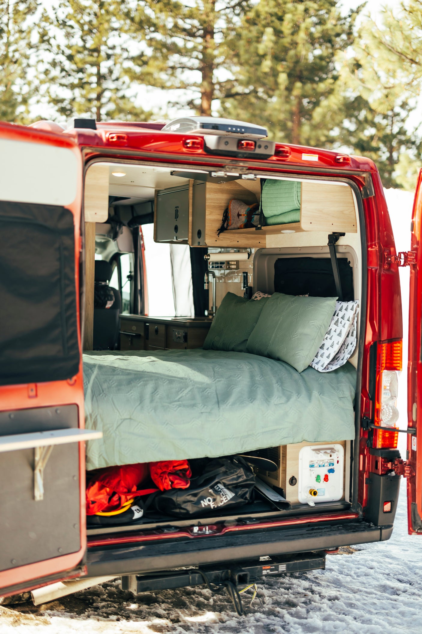 This RV rental shows a camper van's open rear doors, revealing a comfy bed, overhead cabinets, and under-bed storage.