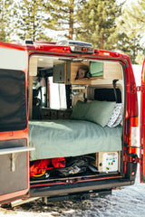 This RV rental shows a camper van's open rear doors, revealing a comfy bed, overhead cabinets, and under-bed storage.