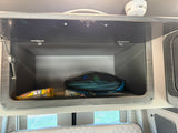 Open overhead storage cabinet in an RV rental. Visible items include a mesh bag, snacks, and small supplies. Great for travel.