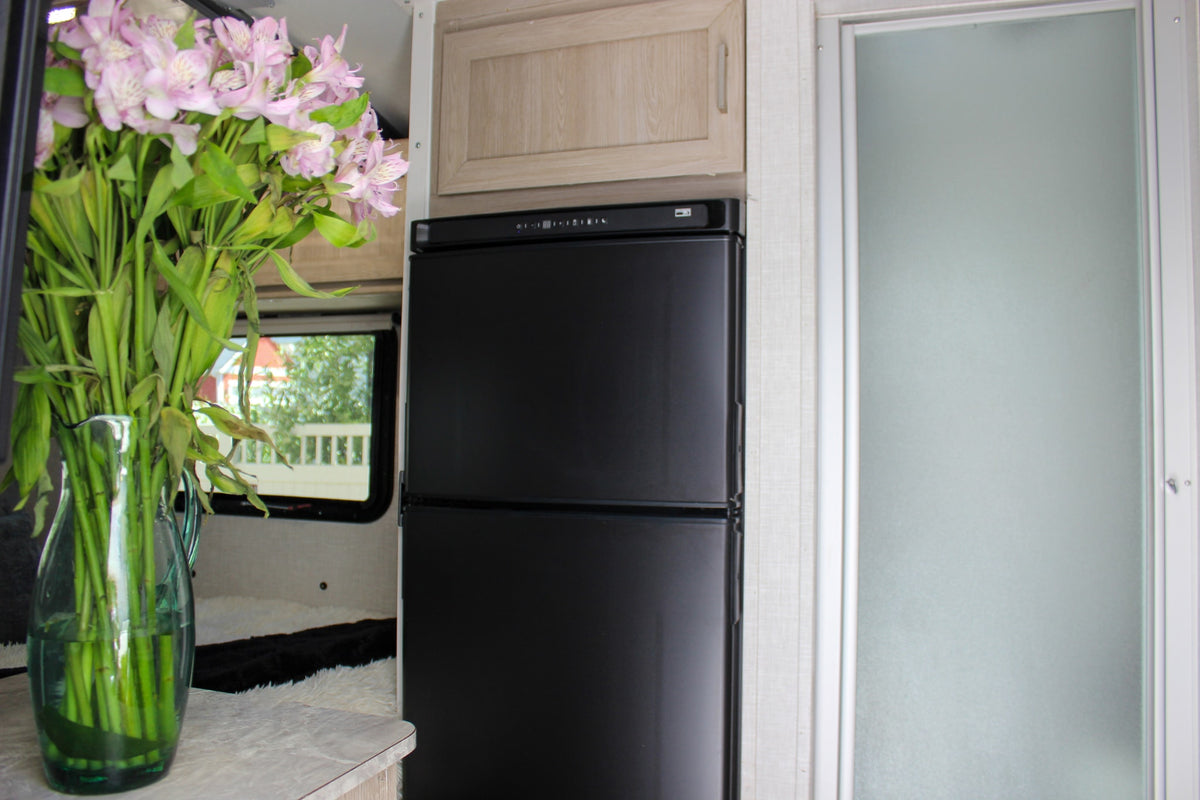 RV rental interior: A vase of pink flowers on a counter, a compact black refrigerator, and a frosted glass door for a cozy travel space. — photo 7