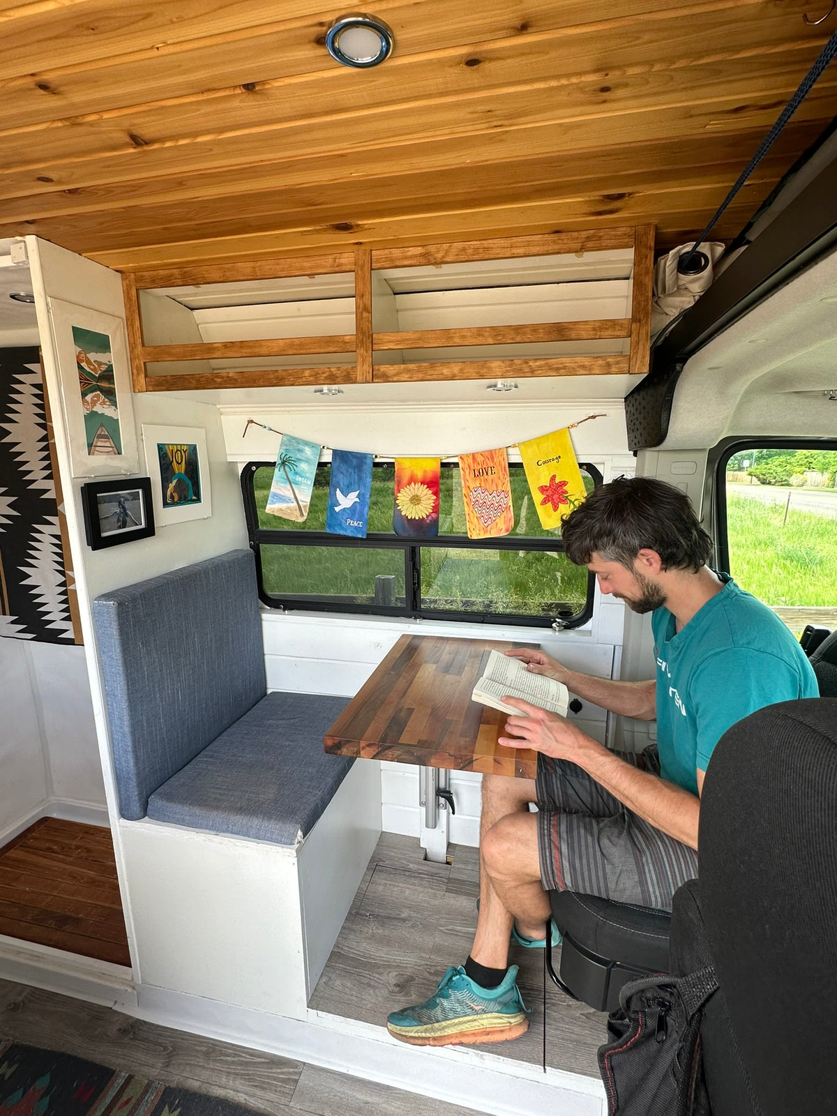 A man reads inside a cozy custom RV rental with wood paneling & built-in seating, ideal for relaxing van life adventures. — photo 5