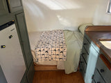 Cozy RV rental interior with a bed, bat-patterned blanket, compact fridge, and a small kitchenette with wooden counters.