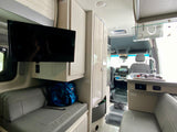 An RV rental's interior, featuring a TV, seating, and kitchenette with a view to the front cabin.