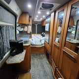 Interior of an RV rental showing a functional kitchen, cozy sleeping area, wood cabinets, and ample lighting.