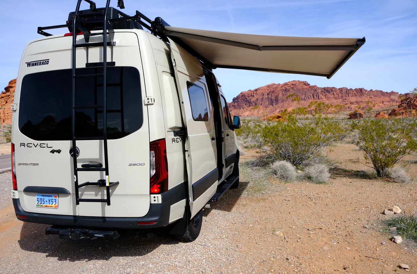 Winnebago Revel rv rental van parked in a desert landscape with red rock formations, its awning extended.