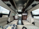 Luxurious rv rental interior featuring comfortable cream seating, rich wood accents, mounted TV, and large windows.