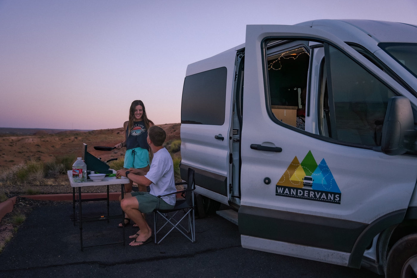 Enjoy outdoor cooking from your RV rental! A couple prepares a meal next to their campervan at twilight in a desert landscape. — photo 11