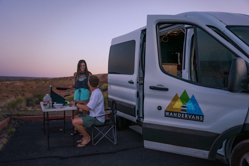 Enjoy outdoor cooking from your RV rental! A couple prepares a meal next to their campervan at twilight in a desert landscape. — photo 11