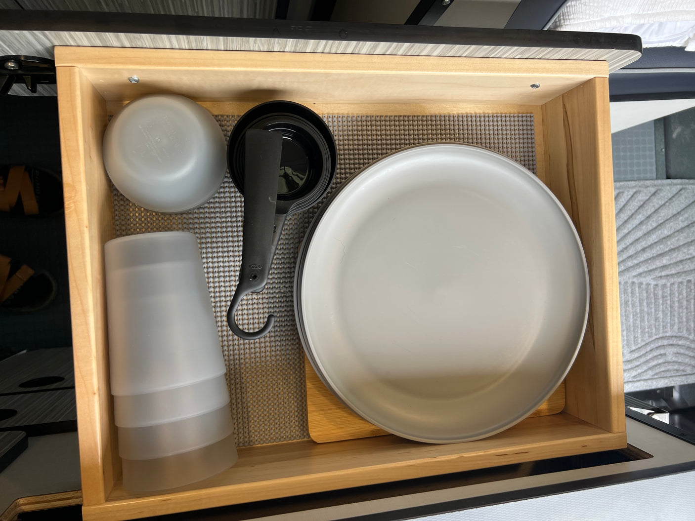 Compact RV rental kitchen drawer with organized plates, cups, bowls, and measuring tools on a grippy mat.