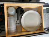Compact RV rental kitchen drawer with organized plates, cups, bowls, and measuring tools on a grippy mat.
