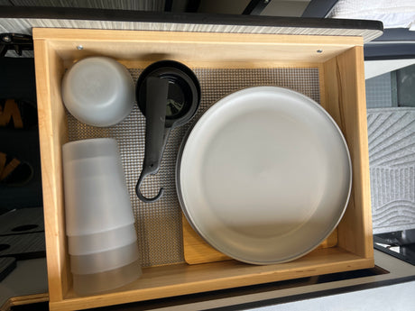 Compact RV rental kitchen drawer with organized plates, cups, bowls, and measuring tools on a grippy mat.