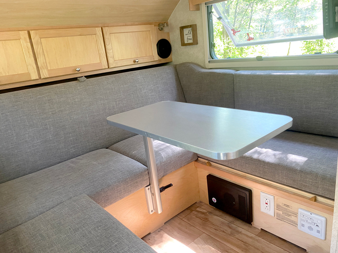 RV rental interior: cozy grey U-shaped dinette with light wood cabinets, an adjustable table, and a window view.