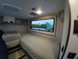 Spacious RV rental interior featuring a long bed, wide window offering an outdoor view, and climate controls.