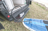 RV rental van powers an electric pump to inflate a paddleboard by the grassy beach. Ready for water adventures!