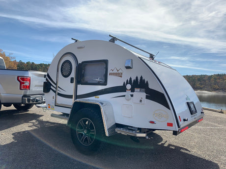 This white Boondock teardrop travel trailer, an ideal RV rental for outdoor adventure, is parked lakeside, ready for camping.
