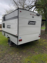 Explore this Coleman travel trailer, ideal for an RV rental adventure. The spacious camper is shown parked on a grassy outdoor area.