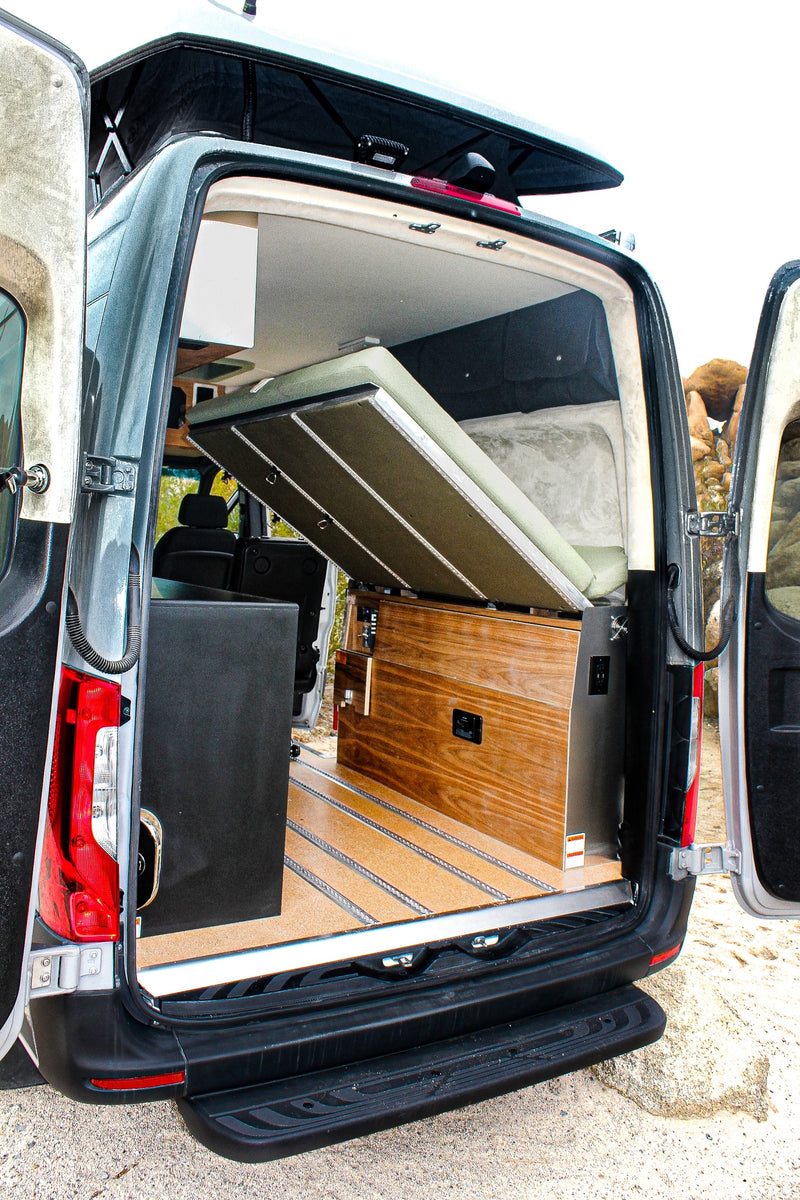Open rear doors of an RV rental reveal its interior with a clever pop-top bed, wooden cabinetry, and durable floor. — photo 12