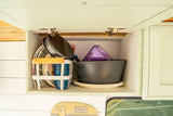 RV rental kitchen cabinet: Organized plates, cups, and cookware in a mint-colored overhead storage.