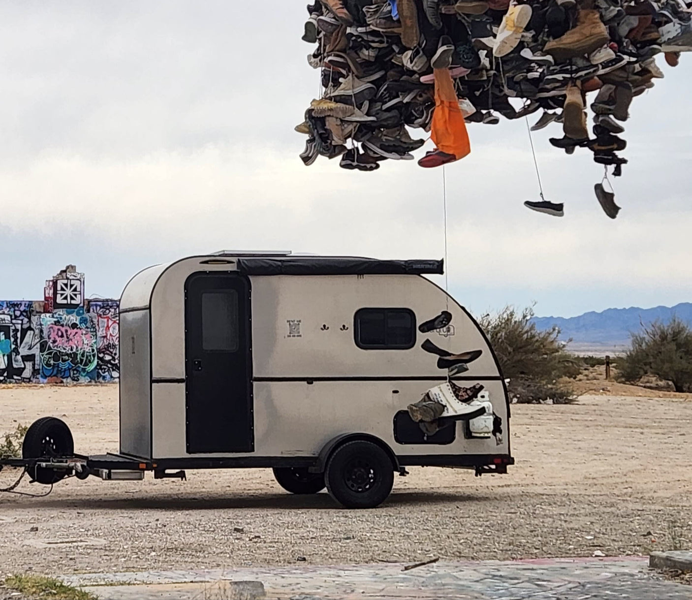 Unique RV rental camper parked near a shoe tree art installation and graffiti walls in a desert. Adventure awaits!|An rv rental