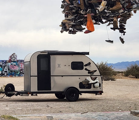 Unique RV rental camper parked near a shoe tree art installation and graffiti walls in a desert. Adventure awaits!|An rv rental