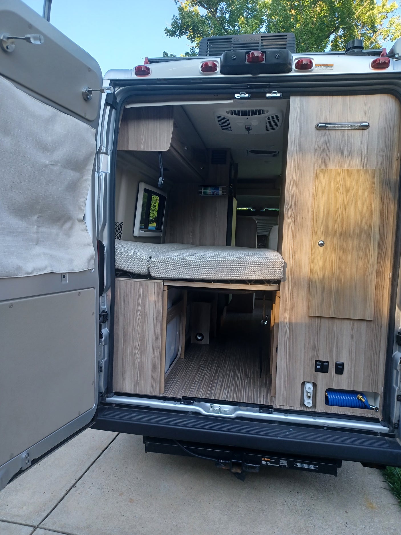 Inside an RV rental looking forward from open rear doors, featuring a multi-functional bed, wood cabinetry, and ample storage.
