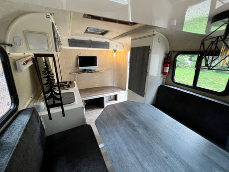 Inside a compact RV rental: modern interior with grey dinette, kitchen, TV, and comfy seating.