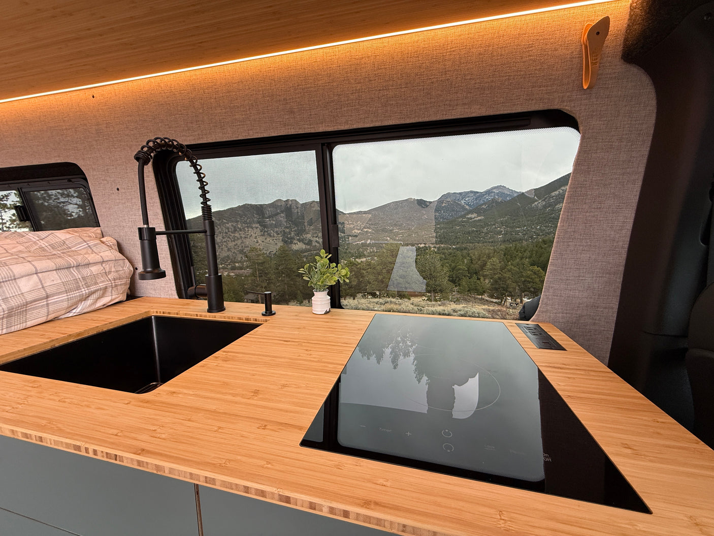 Modern rv rental kitchen with sleek black sink, induction cooktop, bamboo counters, and mountain views outside.