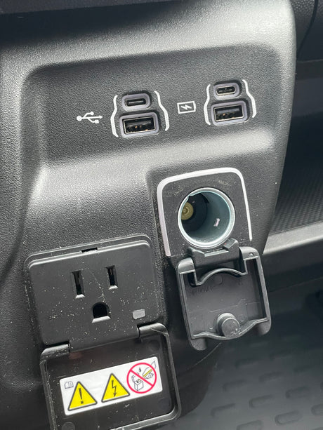 RV rental: Vehicle charging station with USB-A, USB-C, 12V, and a covered 110V AC outlet for electronic devices.