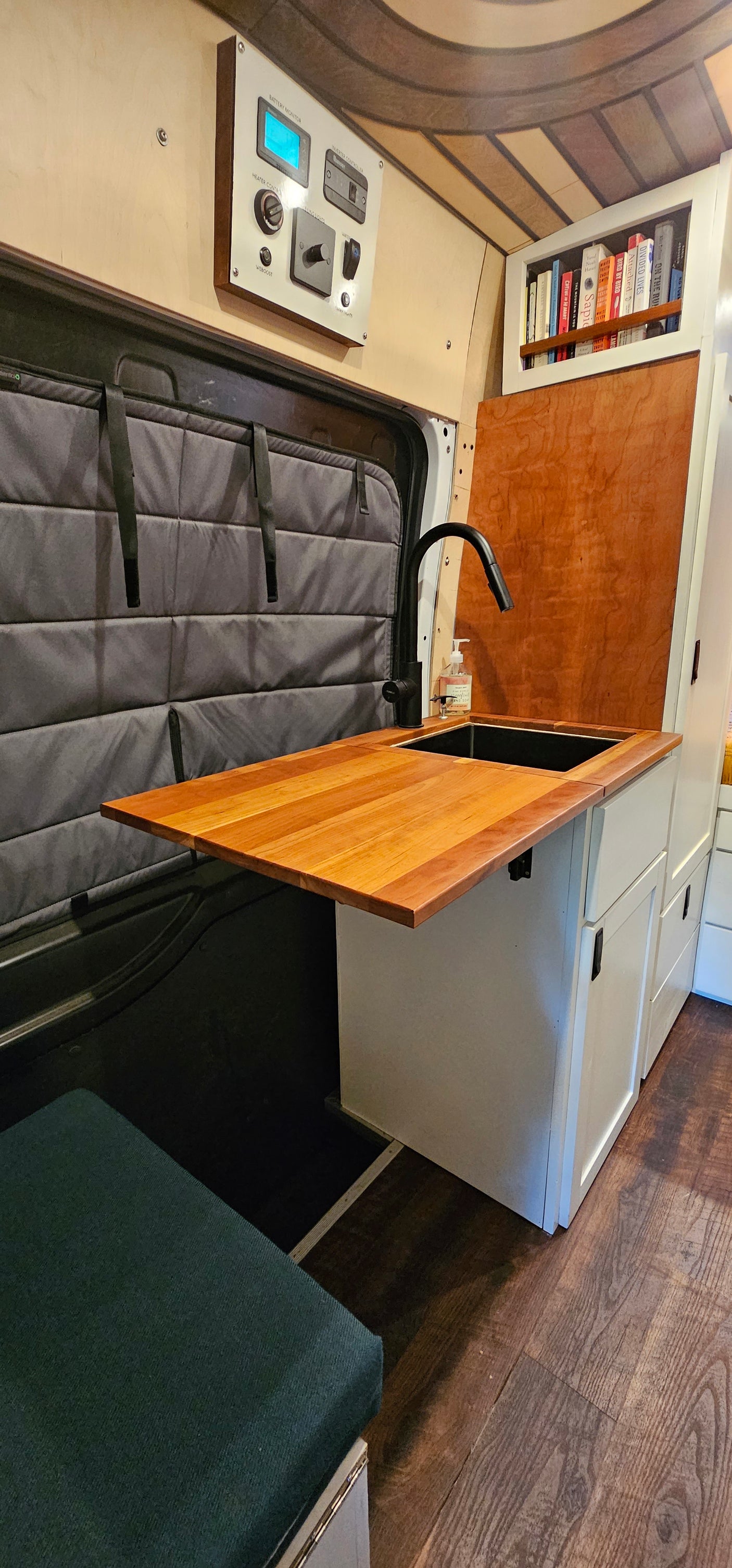 Functional RV rental interior: Kitchenette with sink, smart control panel, and a cozy built-in bookshelf.