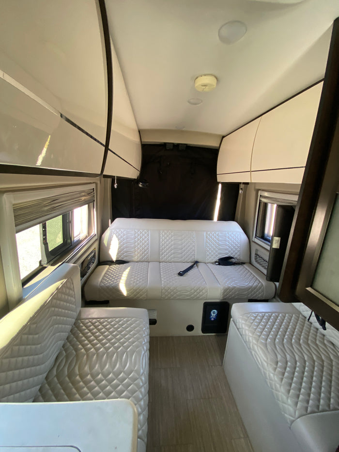 Spacious rv rental interior featuring light quilted seating, overhead storage, and large windows, perfect for travel.