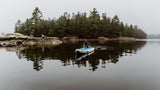Misty lake tranquility: a child paddles on a SUP, another explores rocky shore near a forest. Ideal for an RV rental adventure!