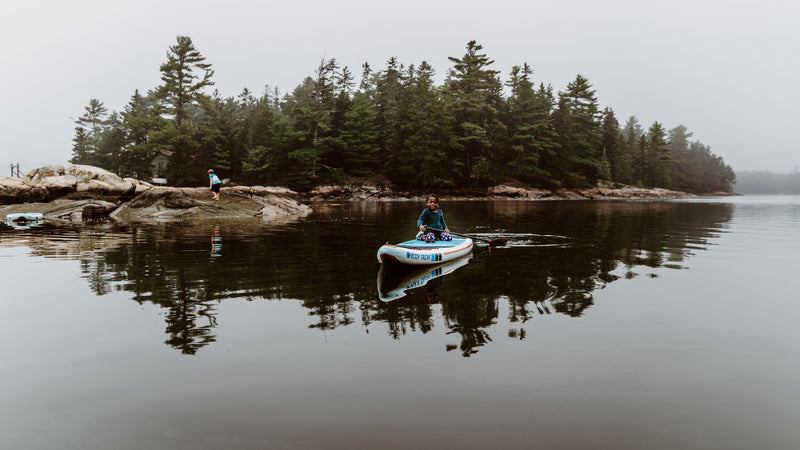 Misty lake tranquility: a child paddles on a SUP, another explores rocky shore near a forest. Ideal for an RV rental adventure! — photo 12