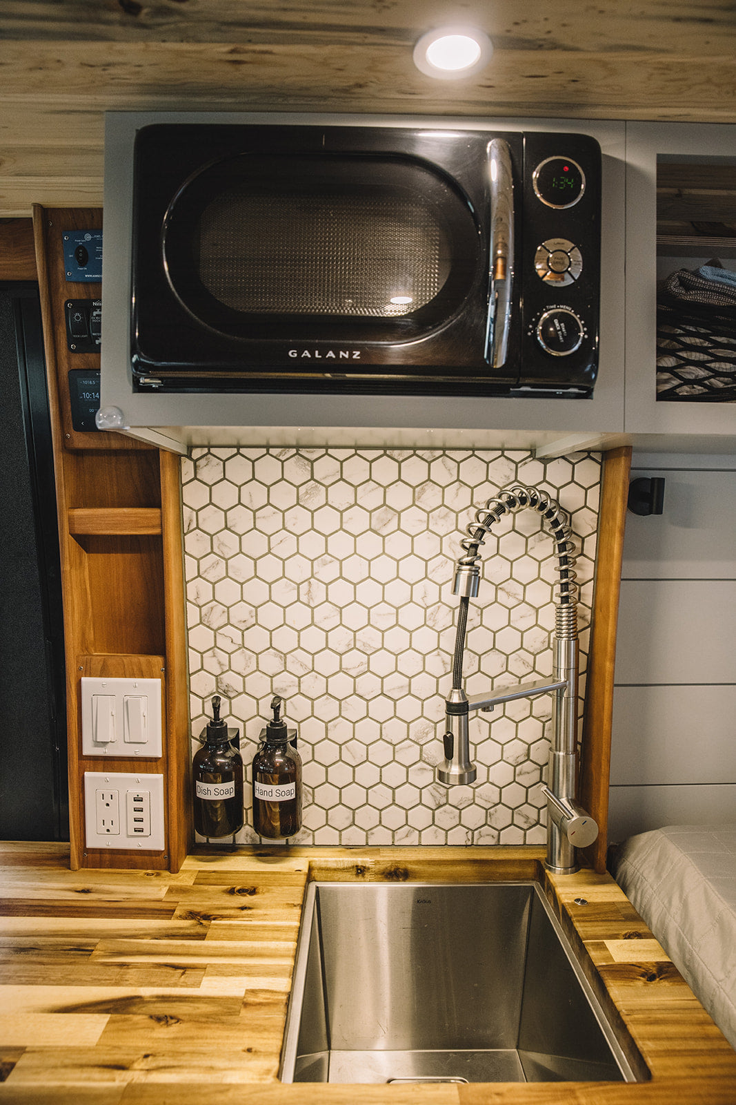 Compact and stylish RV rental kitchen with a Galanz microwave, modern faucet, hexagon tile backsplash, and spacious wood countertop.