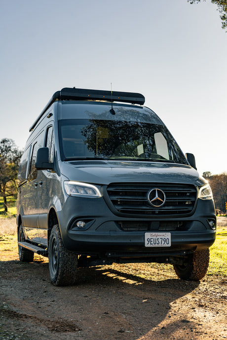 Dark gray Mercedes-Benz Sprinter van, ideal for RV rental off-road adventures, parked on a sunlit dirt path.